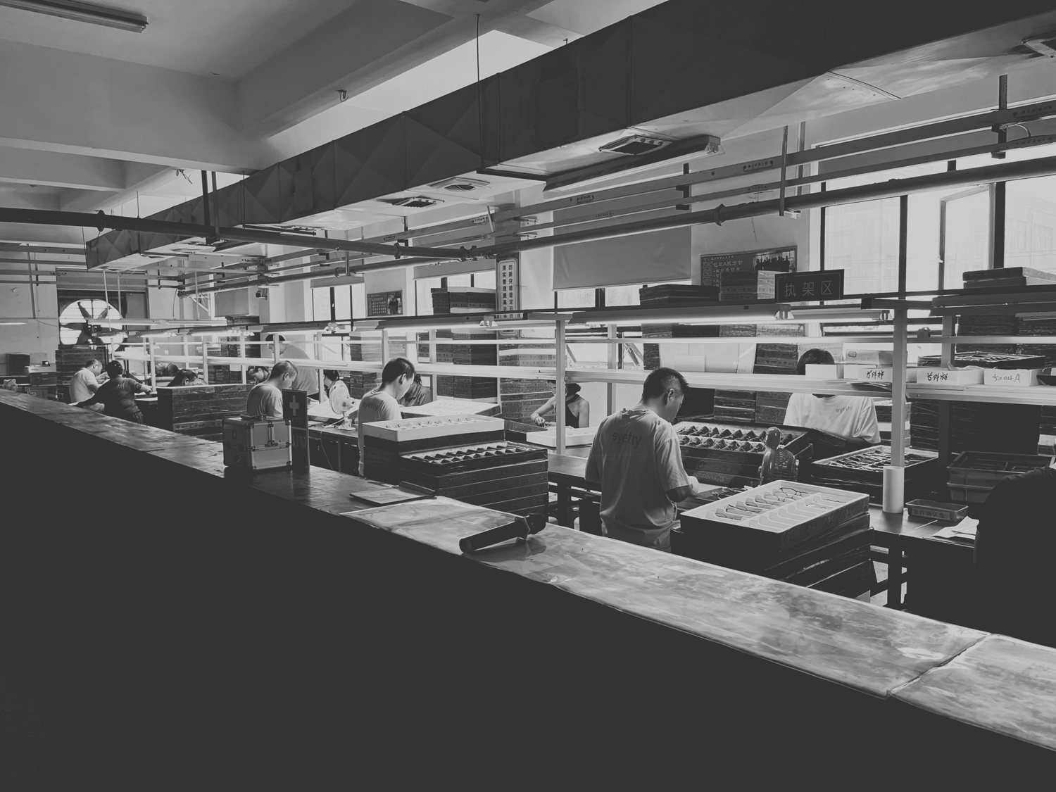 Black-and-white archival photo of an eyewear assembly floor: rows of benches, workers at stations