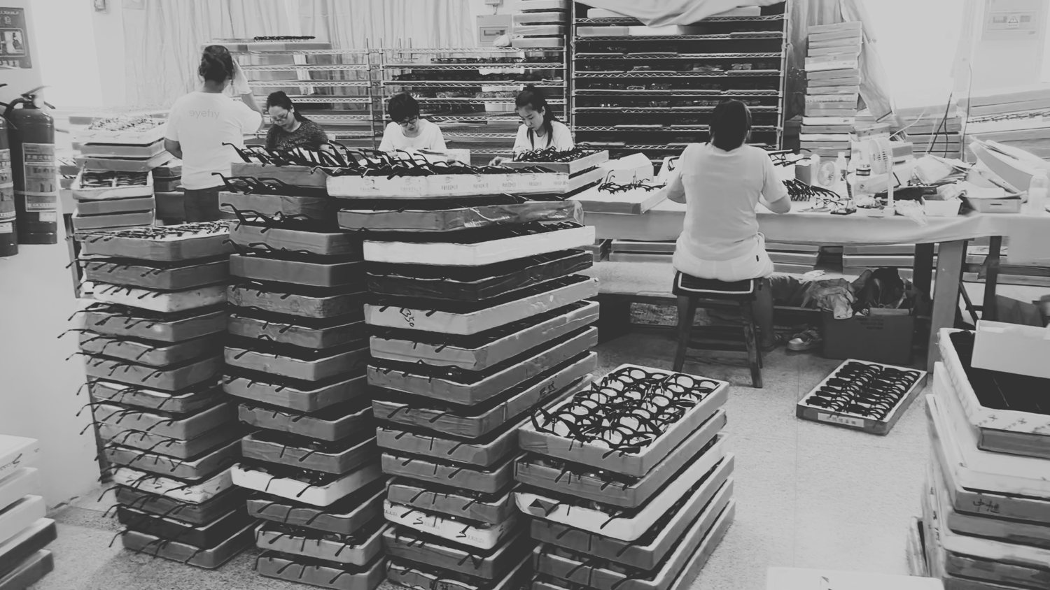 Black-and-white archival photo of a production floor with tall stacks of frame trays between workers