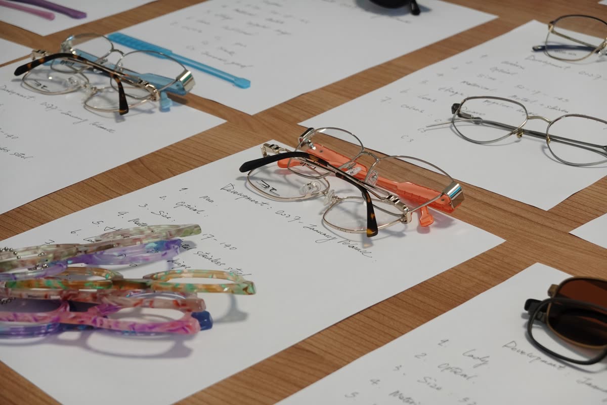Frames resting on handwritten development sheets listing size, material and hinge for each model